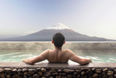Asian man relaxing in outdoor Japanese bath with Mt. Fuji view
