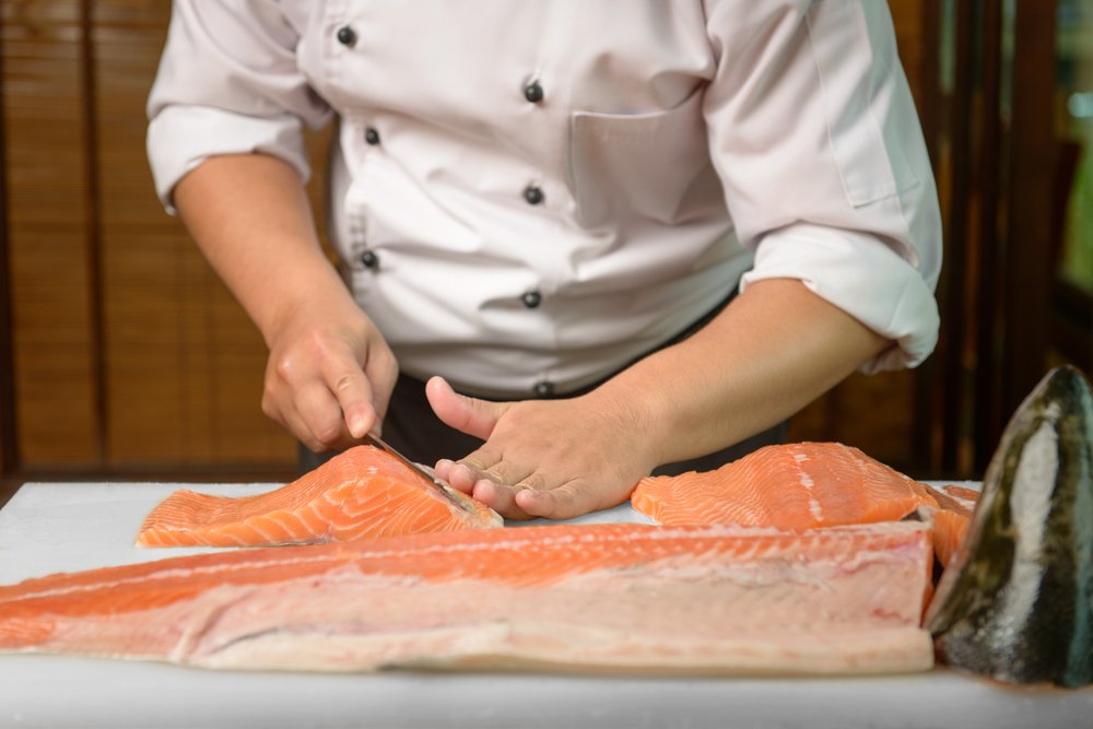 Chef preparing a fresh salmon on a cutting board, Japanese chef in restaurant slicing raw fish for salmon sushi, ingredient for seafood dish