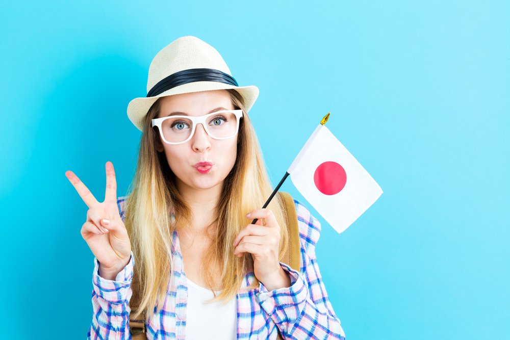 Happy young traveling woman holding Japanese flag